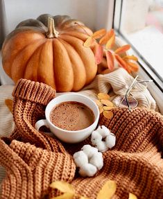 a cup of hot chocolate with marshmallows on a blanket next to a pumpkin