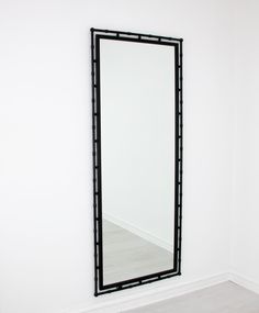 a black framed mirror sitting on top of a white wall next to a wooden floor