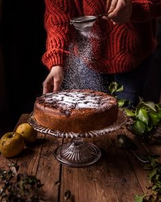 a person sprinkling sugar onto a cake on top of a wooden table next to lemons