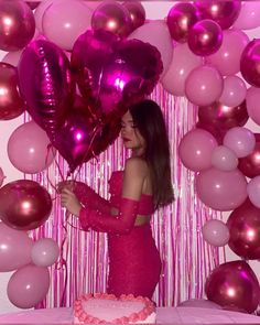 a woman standing in front of a cake with pink and purple balloons on it,