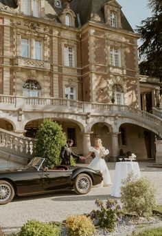 a bride and groom standing next to an old fashioned car in front of a large building