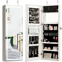 a white closet with jewelry hanging from it's sides and a bed in the background