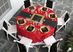 a red table with black and gold place settings is set for an elegant dinner party