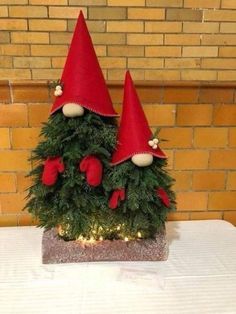 two christmas trees with red hats and lights on them are sitting on a white table