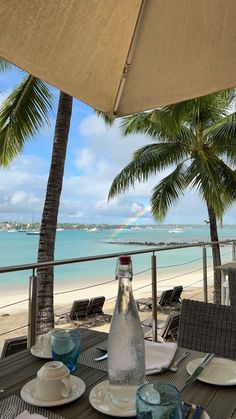 the table is set for two on the balcony overlooking the beach and ocean with palm trees