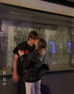 a young man and woman kissing in front of a store window with graffiti on it