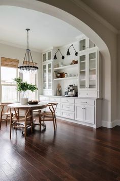 a dining room table and chairs in front of a large window with open shelving