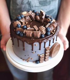 a person holding a cake with chocolate and blueberries on it