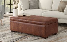 a living room with a white couch and brown footstool in front of a window