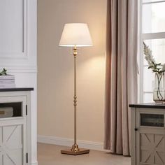 a floor lamp with a white shade on it in front of a window and table