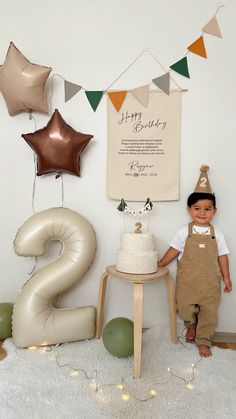 a young boy sitting in front of a birthday cake with balloons and decorations around him