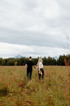 a man and woman holding hands walking through tall grass