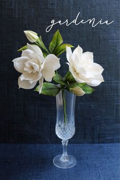 a clear vase filled with white flowers on top of a blue cloth covered tablecloth