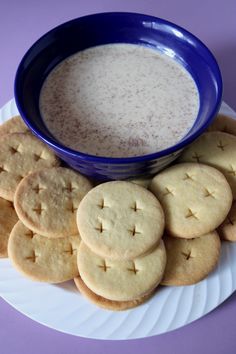 a plate full of cookies next to a bowl of milk on a purple tablecloth