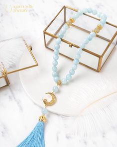 the blue beaded necklace is next to a glass box with a gold plated charm