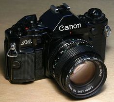 a camera sitting on top of a wooden table next to a black lens with the word canon written on it