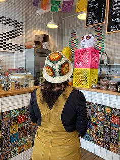 a woman wearing a hat standing in front of a counter with colorful tiles on it