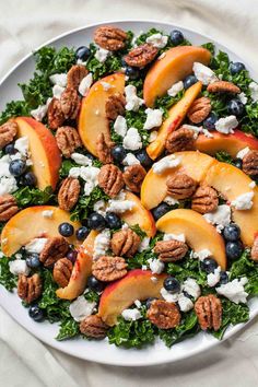 a white plate topped with peaches, blueberries and pecans on top of lettuce