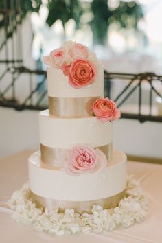 a three tiered wedding cake with pink flowers on the top and gold trimmings