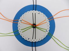 a white clock with orange and green wires connected to it on a blue circular surface