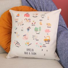 a white pillow with farm animals and words on it sitting on a couch next to pillows