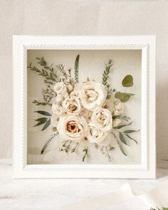 a white frame with flowers in it on a table next to some ribbon and scissors