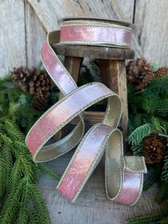 pink and silver ribbon with pine cones in the background on a wooden stand next to evergreen branches