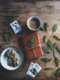 an open book sitting on top of a wooden table next to a cup of coffee