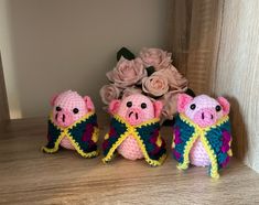 three small crocheted pigs sitting next to each other on a wooden table with flowers in the background