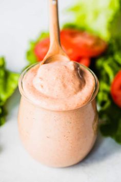 a spoon in a jar filled with dressing next to some lettuce and tomatoes