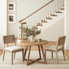 a table with two chairs and a vase on it in front of a stair case