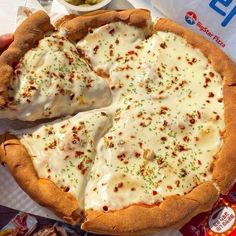 a person holding a pizza with cheese and toppings on it in front of some chips