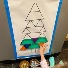 a child is drawing a christmas tree on a white board with blue trimmings