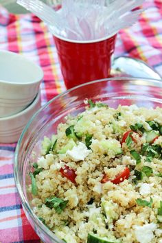 a bowl filled with rice and vegetables on top of a checkered table cloth next to a cup