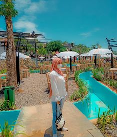 a woman wearing a face mask standing in front of an outdoor garden area with tables and umbrellas