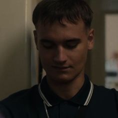 a young man is looking down at his cell phone while wearing a black polo shirt