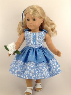 a doll with blonde hair wearing a blue dress and holding a white flower in her hand