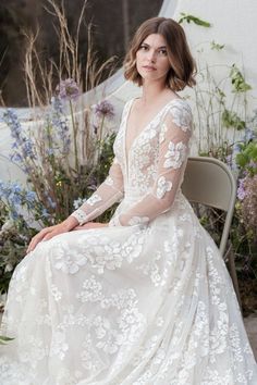 a woman sitting on top of a chair wearing a dress with flowers in the back