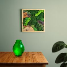 a green vase sitting on top of a wooden table in front of a framed painting