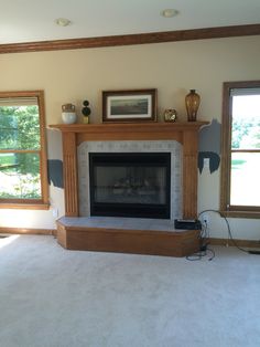 an empty living room with a fireplace and two windows in the corner, all white carpet