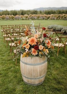 a wooden barrel filled with lots of flowers on top of a grass covered field next to rows of chairs