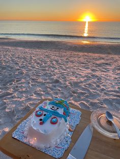 a birthday cake sitting on top of a wooden table next to the ocean at sunset