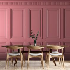 a dining table with four chairs and a vase on it in front of a pink wall