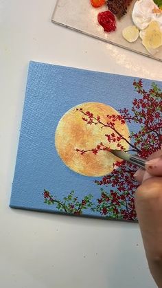 a person is using scissors to paint a painting on a canvas with flowers and fruit