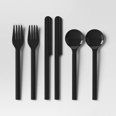 black utensils and spoons are lined up on a white surface with one fork in the middle