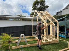 a man standing in front of a wooden frame on top of grass next to a house