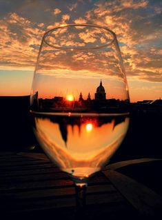 a glass of wine sitting on top of a wooden table next to a sky filled with clouds