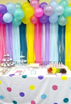 a table topped with lots of balloons next to a wall filled with colorful streamers