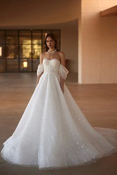 a woman in a white wedding dress standing in an empty room with her hands on her hips