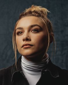 a woman with blonde hair wearing a black jacket and white turtle neck sweater, looking off to the side